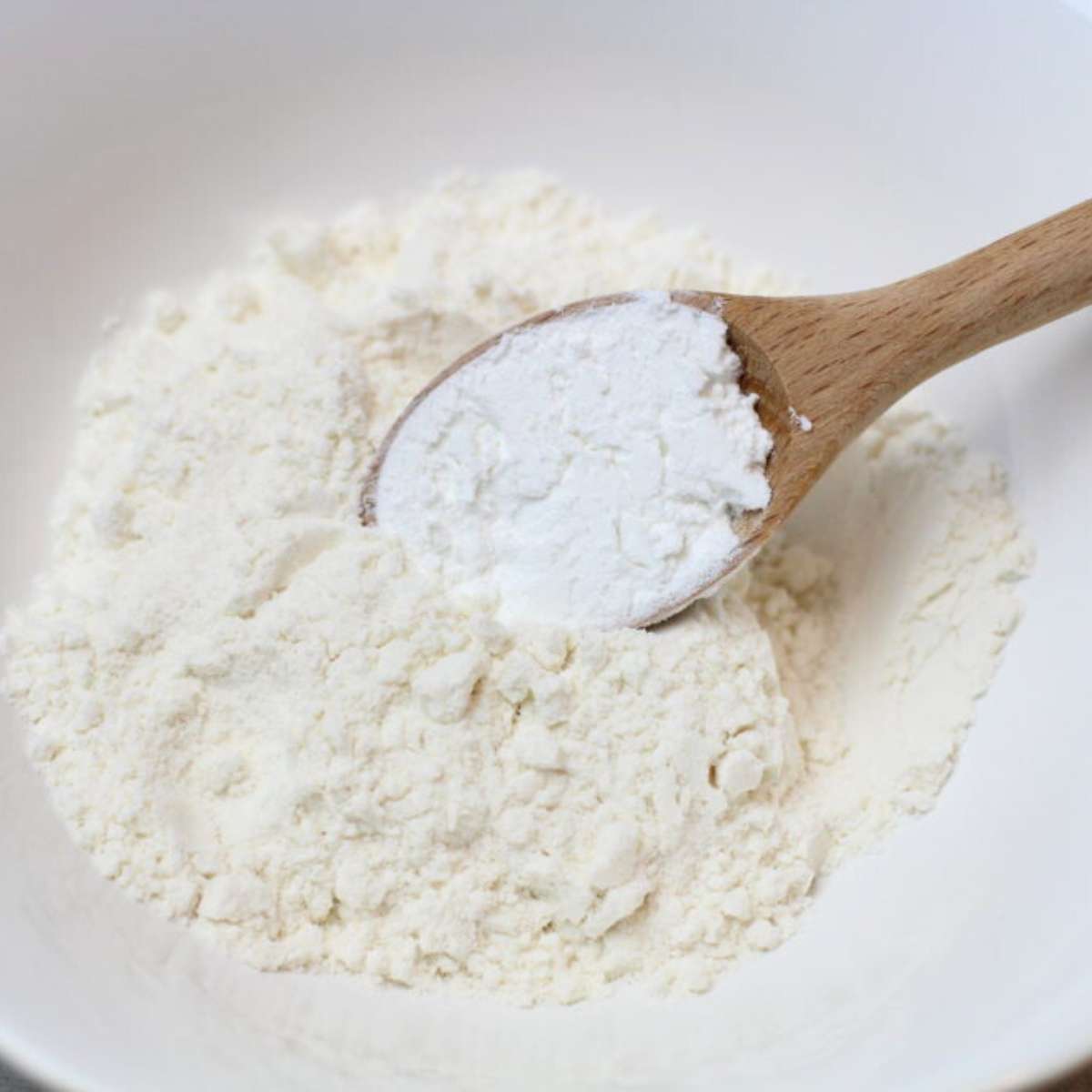 Dry ingredients being mixed together for a green chili egg casserole recipe. A white bowl contains flour, salt and baking powder with a wooden measuring spoon resting neatly inside. 