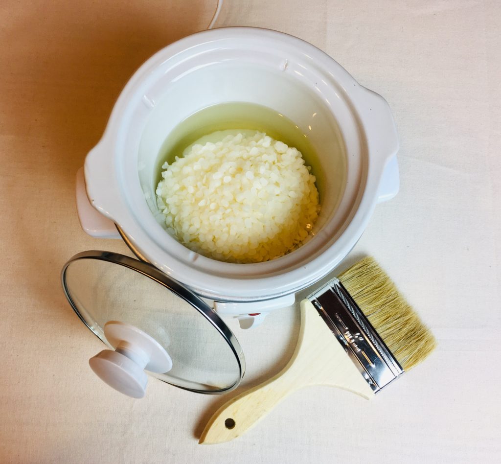 A mini crockpot that contains beeswax pellets and paraffin wax is beginning to melt to make waxed cotton canvas fabric.