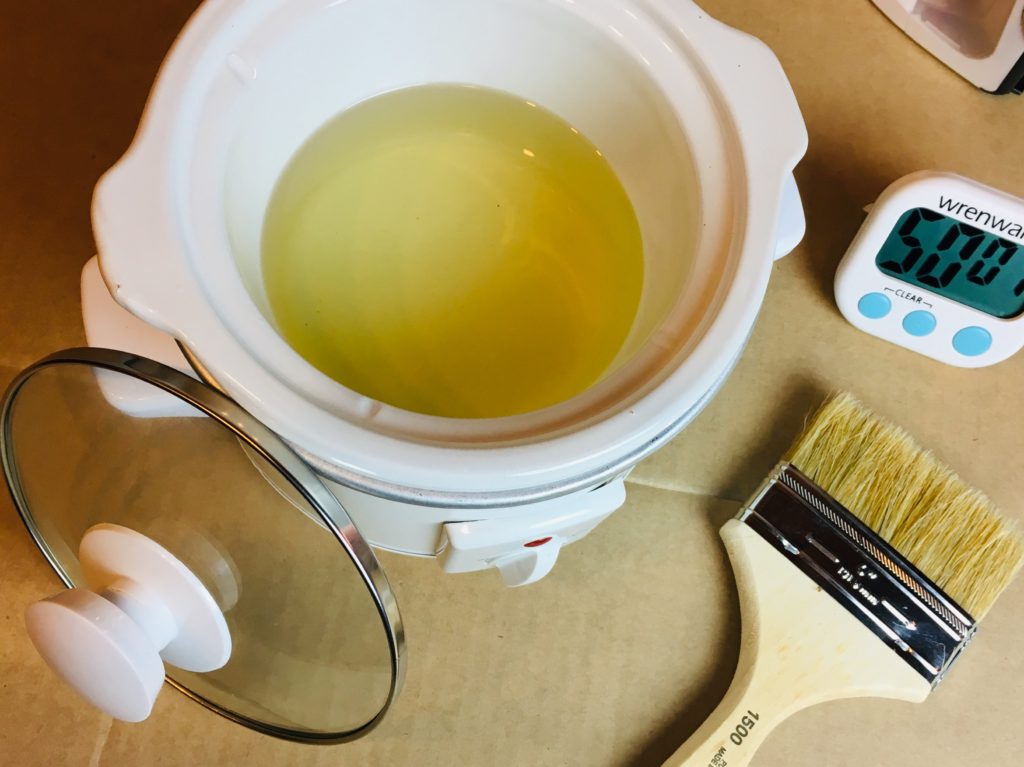 A mini crockpot full of a golden yellow liquid. This is a mixture of beeswax and paraffin that is used to demonstrate how to make waterproof waxed cotton canvas fabric.