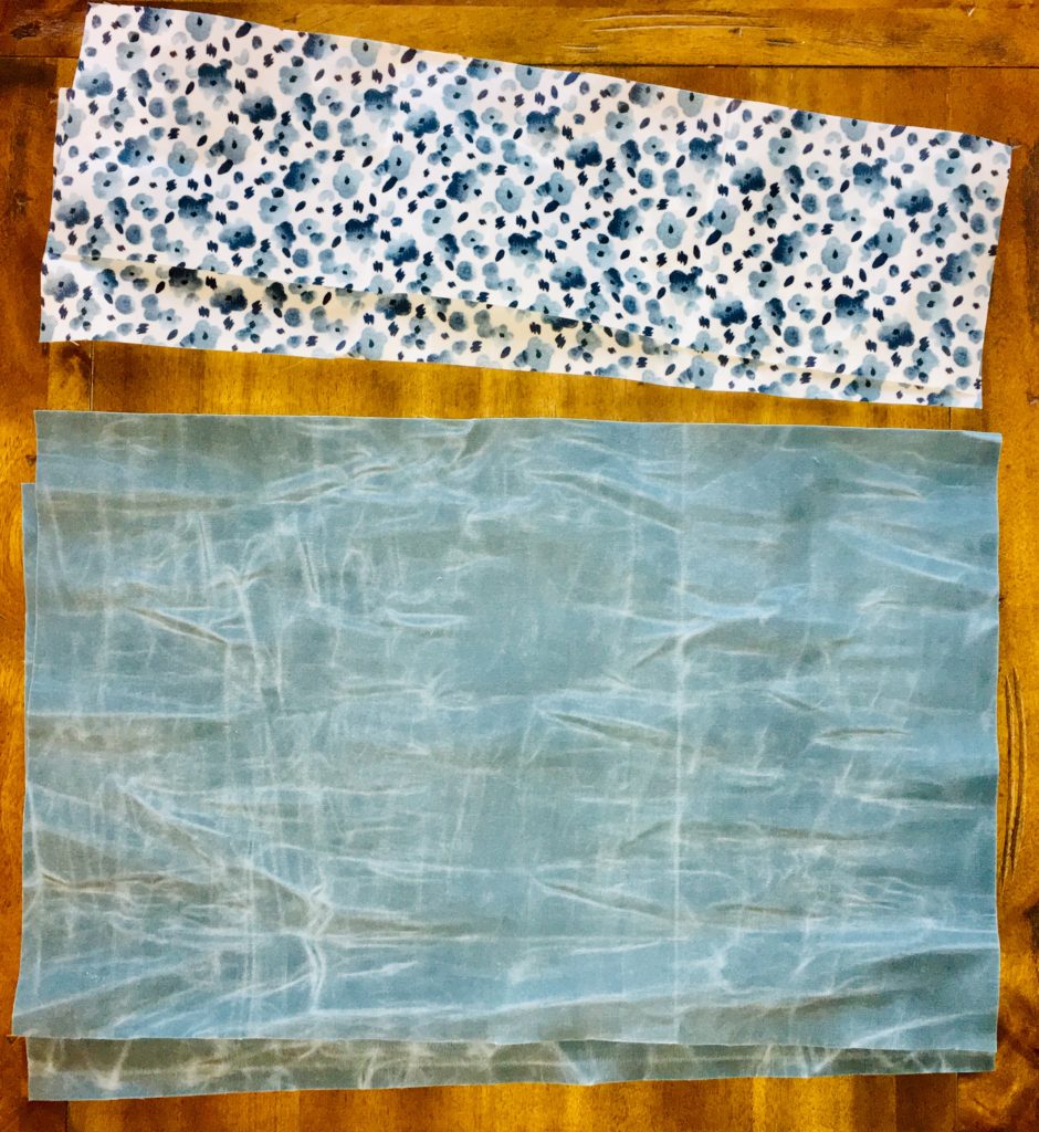 A floral piece of blue and white printed canvas fabric sitting next to pieces of steel gray blue canvas fabric that has already been waxed. 