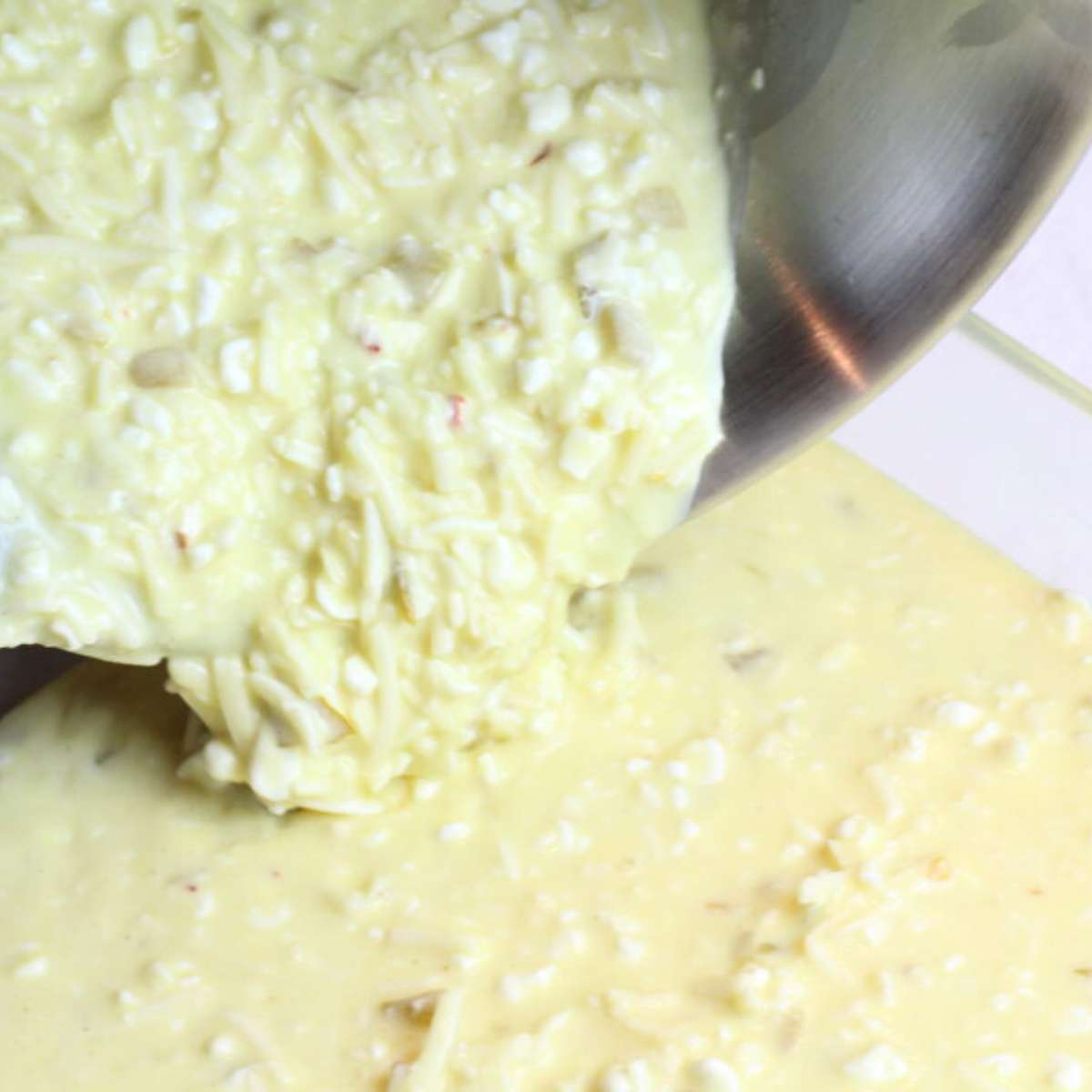 Slowly pouring the egg mixture into the pre-greased clear baking dish. The green chiles, cottage cheese and pepper jack cheese are visible in the mix.