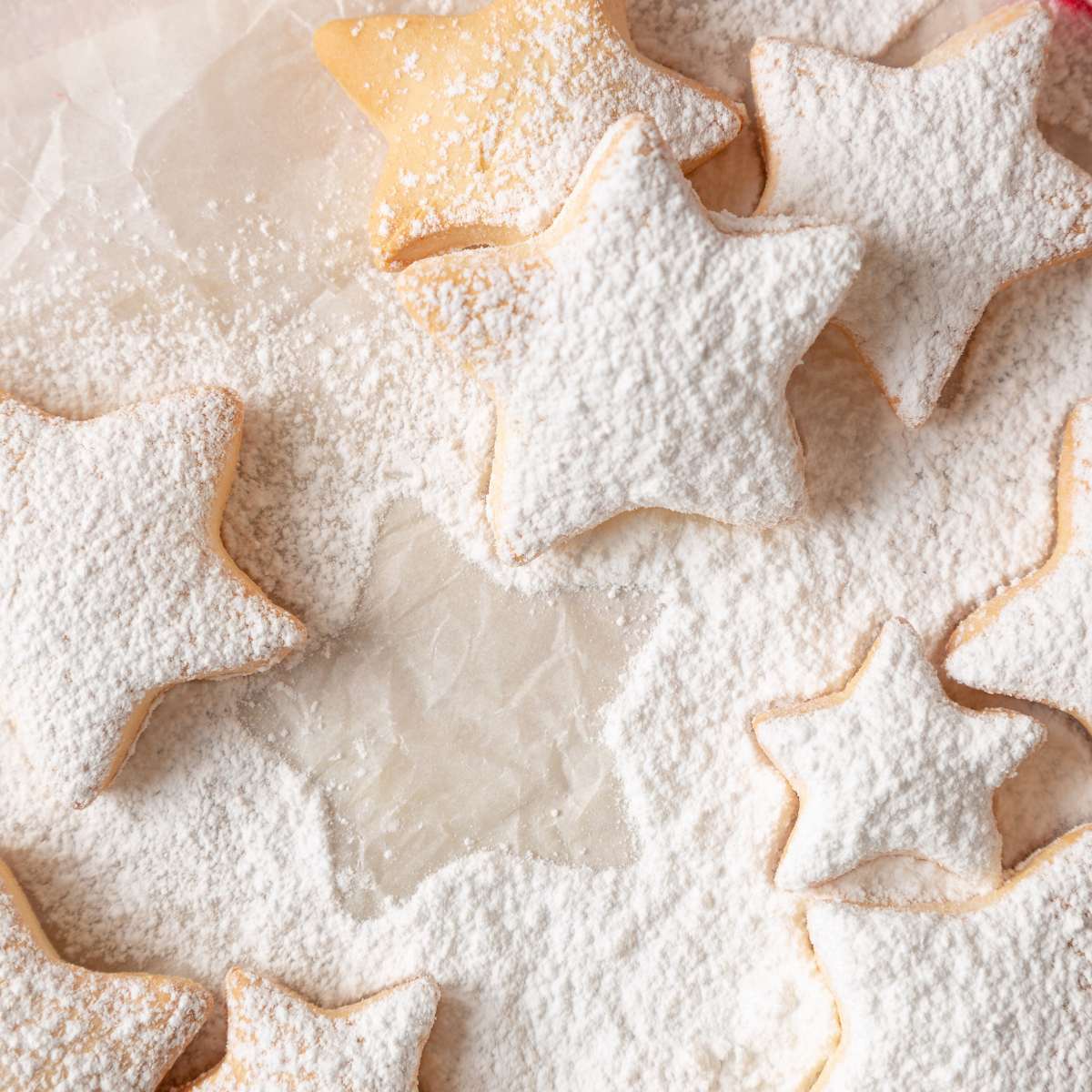 A table dusted with white powdered sugar with star shaped sugar cookies.