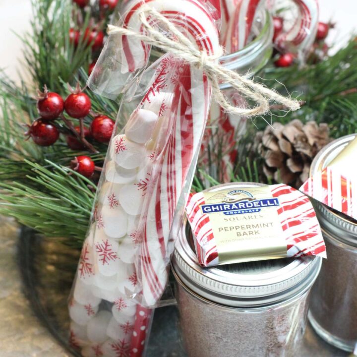 Jars of homemade hot chocolate mix in mason jars ready to be gifted for the holidays. Jars are topped with peppermint chocolates and candy canes.