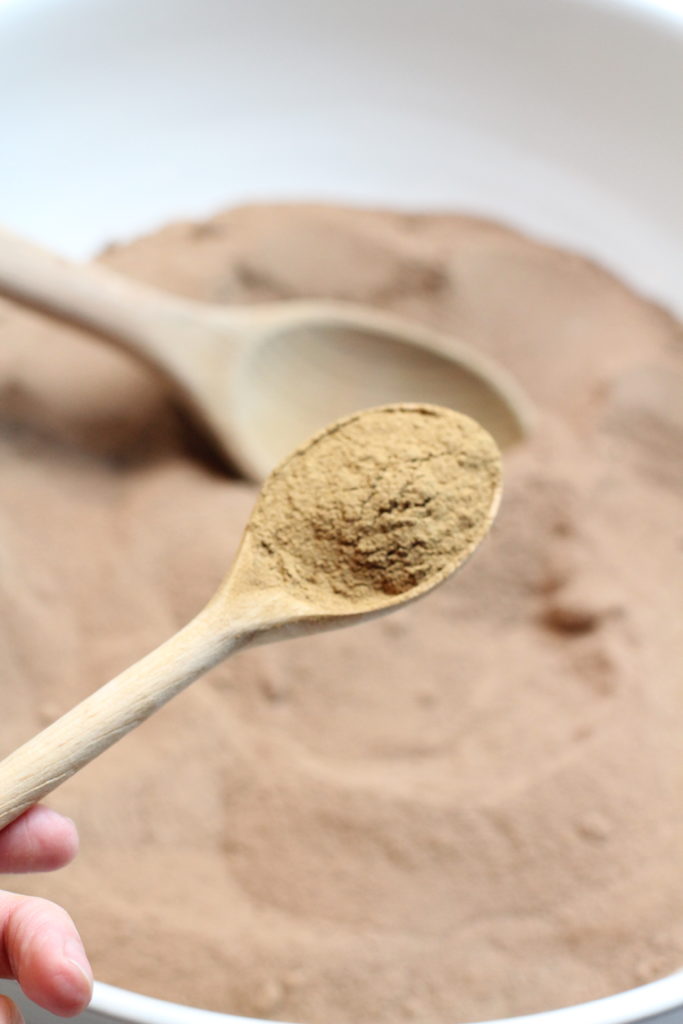 A wooden spoon is holding a scoop of hot cocoa mix powder.