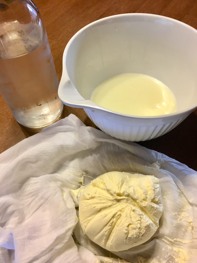 A clear bottle of chilled water sitting next to a bowl of buttermilk and a fresh made ball of homemade food processor butter sitting on a white tea towel.