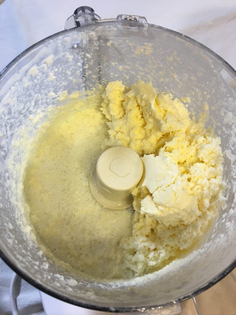 Homemade food processor butter progress picture. This picture shows after the heavy whipping cream has been churning for 8 minutes. The solids have separated from the creamy yellow butter solids now.