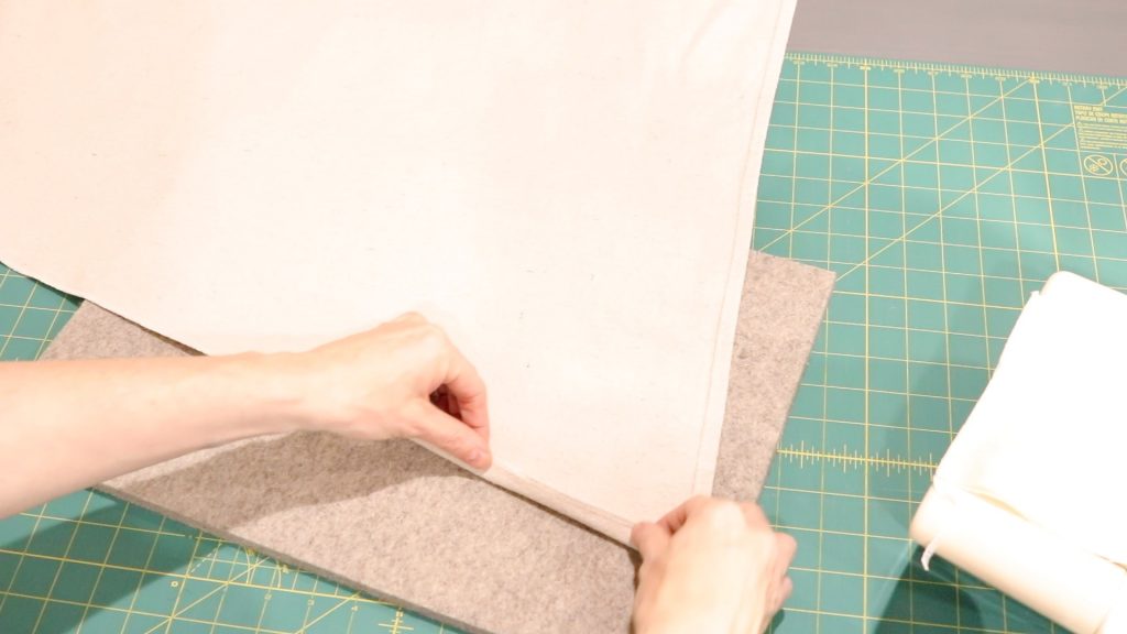 A woman is folding the edge of the canvas demonstrating how you can achieve the same look on your DIY hammock chair without a serger sewing machine. She is carefully folding the edges under before sewing. 