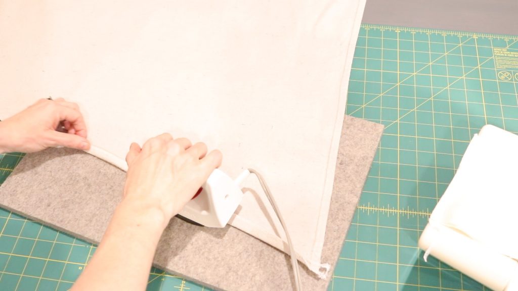 A woman is holding a small iron and pressing her fabric along the edge. 