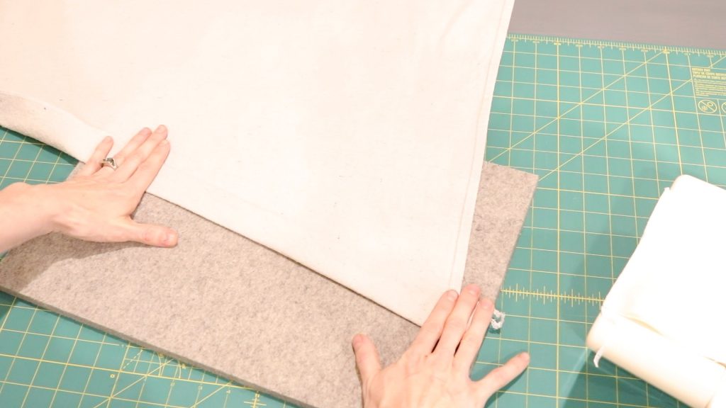 A woman is folding up the edge another time to enclose the raw edge of the canvas fabric without the need for a serger sewing machine. 