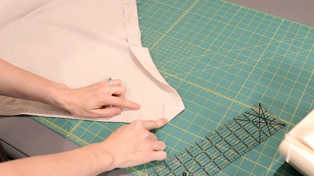 A hand is pointing to the tail of the fabric showing how to enclose it before sewing. 