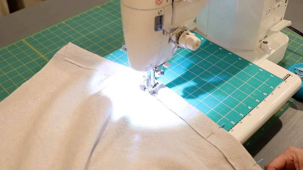 A piece of tan canvas fabric sitting under the presser foot of a white sewing machine.