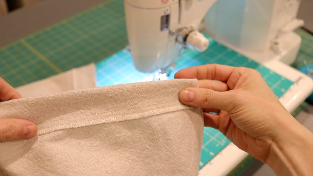 Showing a piece of fabric that has been sewn twice for reinforcement. A white sewing machine is in the background.