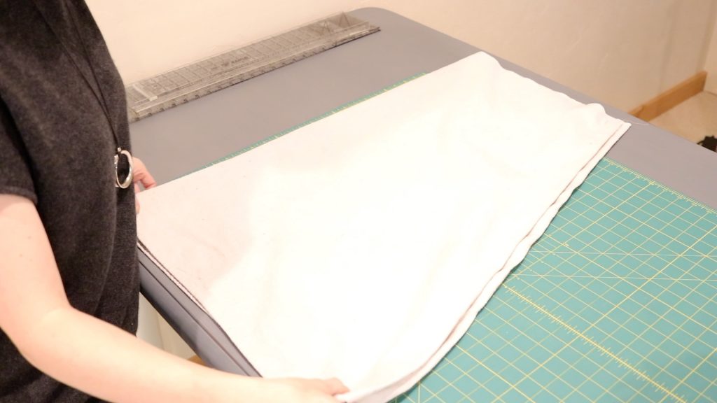 The folded cloth for a DIY sky chair resting on a cutting table preparing for the next step of the project. A woman folding the fabric is wearing a black shirt.