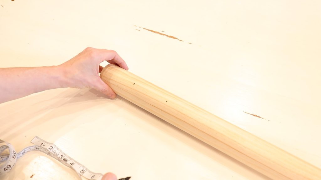 A hand holding a wooden dowel rod that has been marked with a black sharpie marker for drilling.