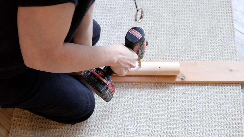 A woman is drilling two holes along the edge of a wooden bowl rod. 