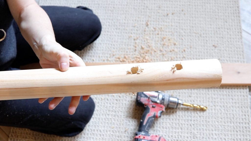 A freshly drilled piece of wooden dowel with two holes drilled on one end.