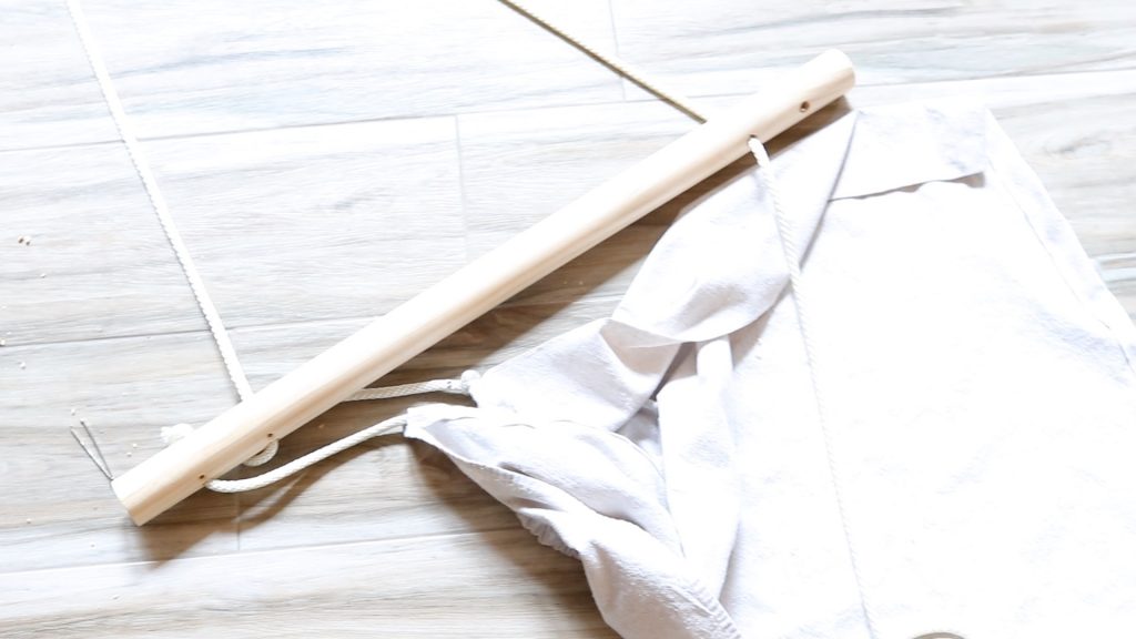 A picture of a cream canvas sky chair that is being constructed. A white rope is attached to the dowel rod where there chair will swing from.