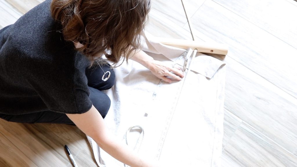 A woman is using a white sewing tape measure to measure a length of rope for her hammock chair. She is measuring to be sure that the length of rope is the same length on both sides of her DIY hanging chair.