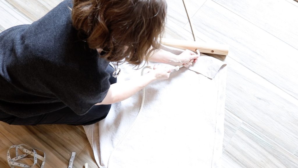 A woman wearing black is tying a knot in a piece of white rope. The rope is being tied to be sure it doesn't come out of the hanging chair.