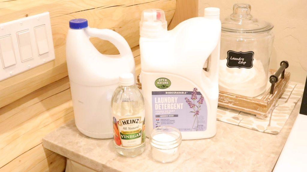 Laundry soap, bleach, vinegar and baking soda used to wash the canvas fabric prior to sewing. The bottles of detergent are sitting on a cream marble counter top in a laundry room. 