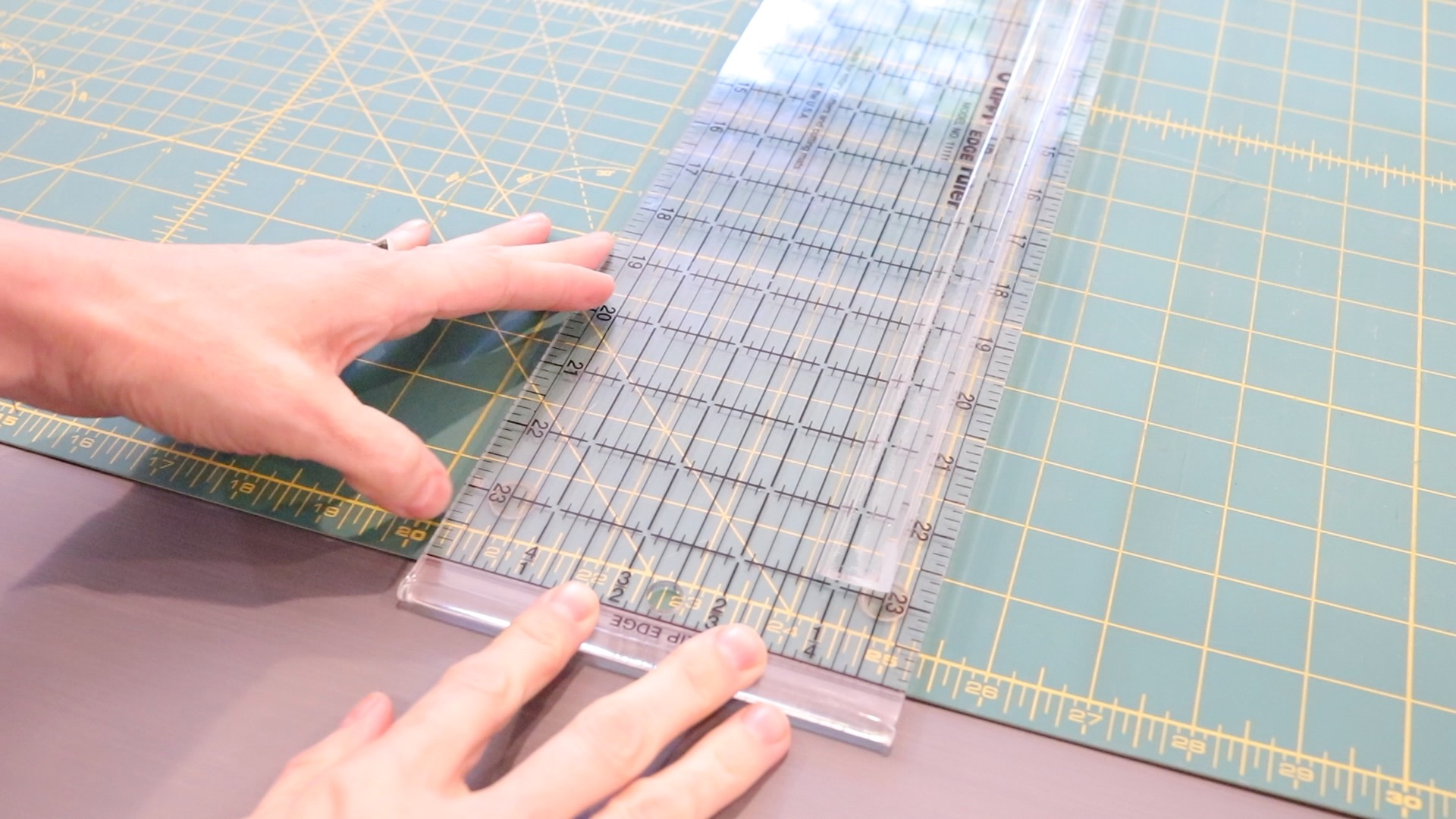 A clear acrylic sewing ruler sitting on a green cutting mat to demonstrate the function of the lip edge on the ruler.