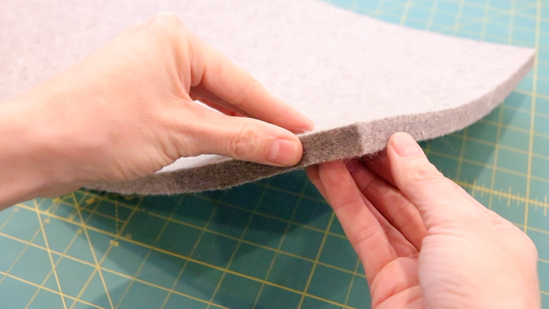 Two hands holding the edge of the gray pressing mat showing the thickness of the mat.