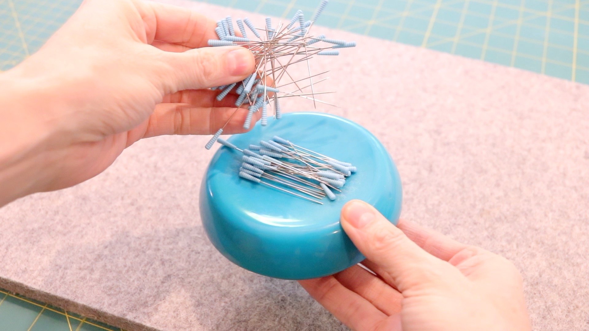 A round turquoise magnetic sewing pin cushion holding a handful of sewing pins with blue tops. 