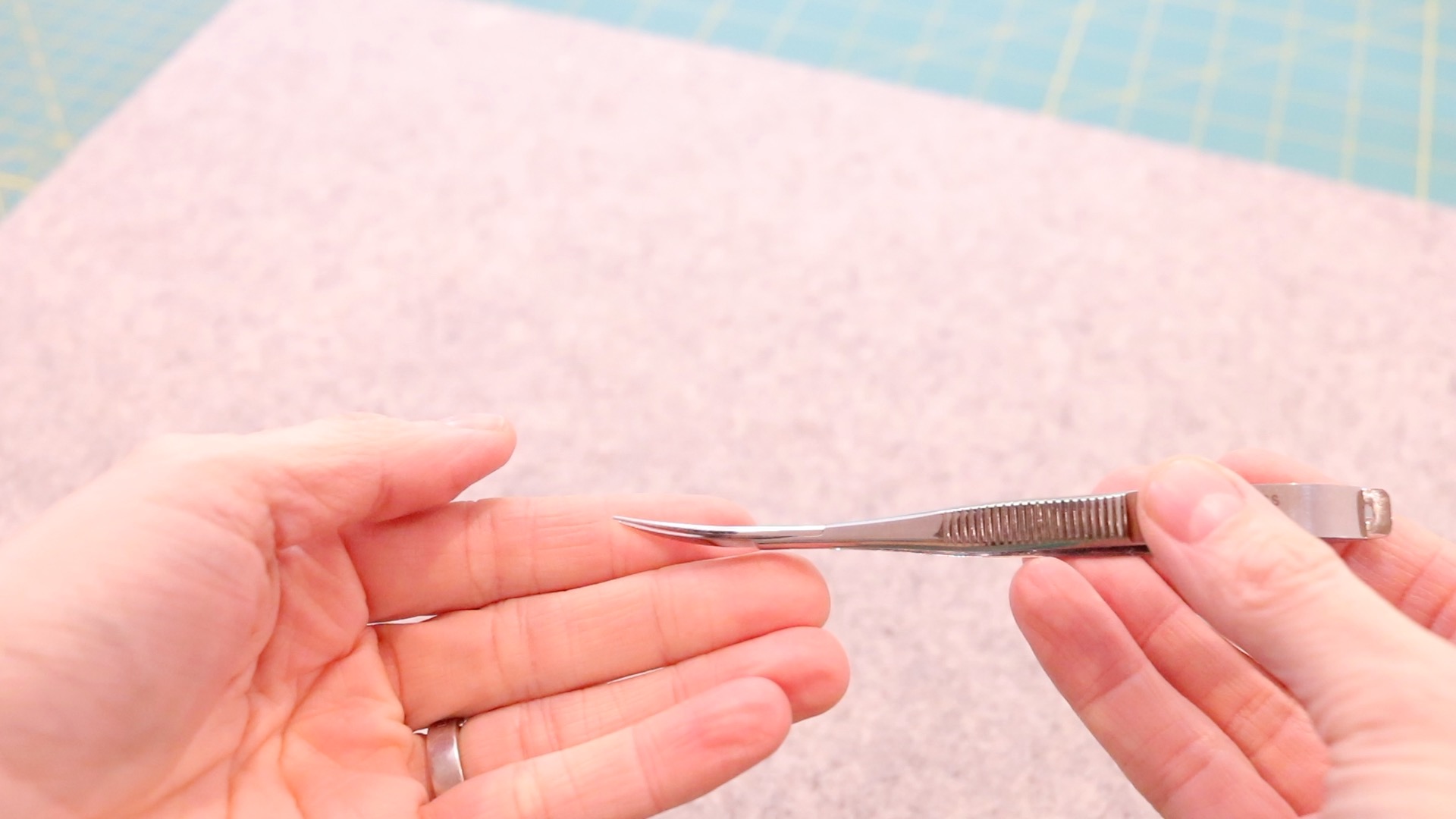 A pair of mini metal thread snip being held up to show the curved design of the mini scissor blades. A gray wool pressing mat is behind.