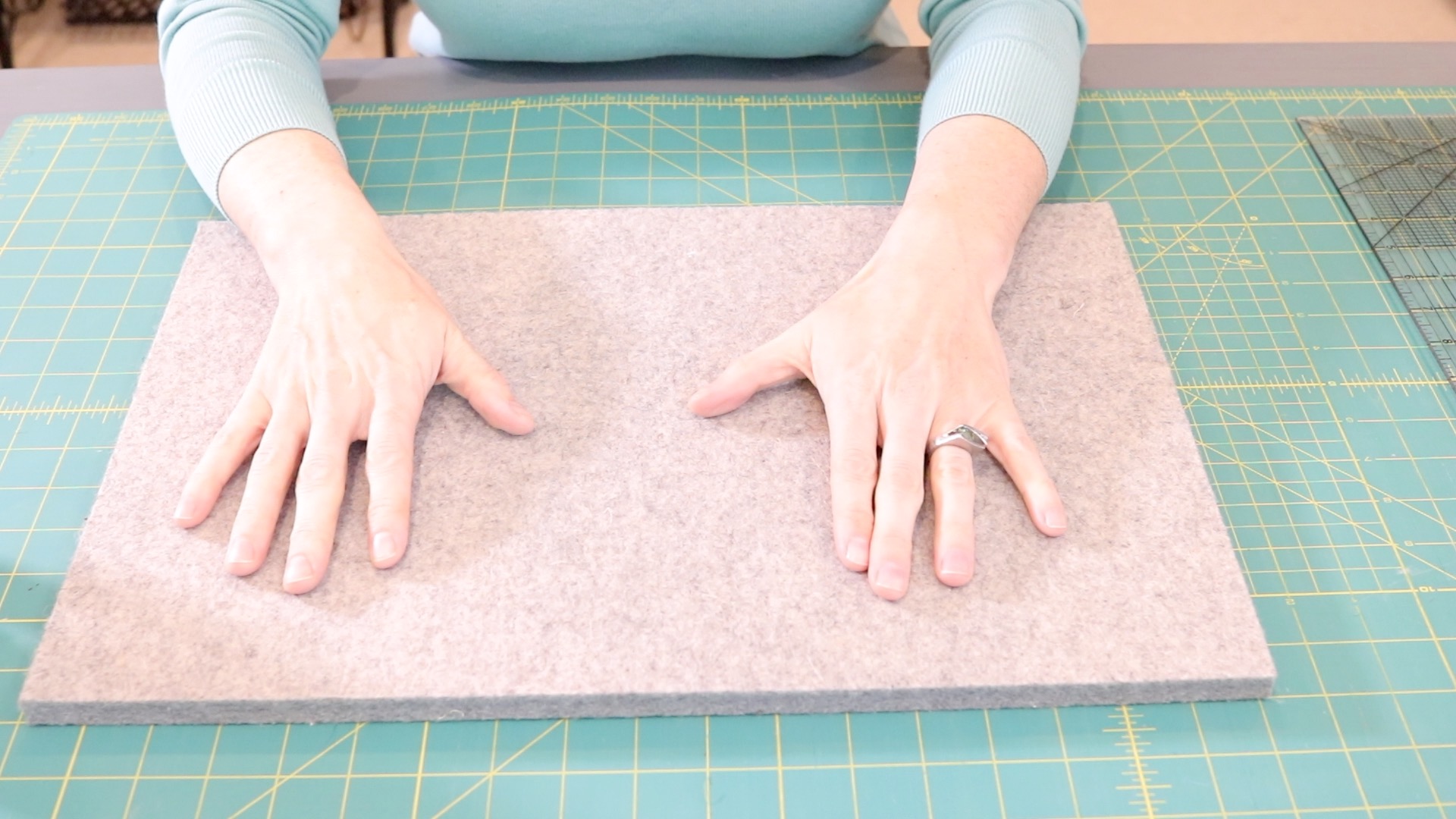 A woman's hands resting onto of a gray wool pressing mat. The pressing mat is resting onto of the green Olfa cutting mat with yellow grid lines on it.