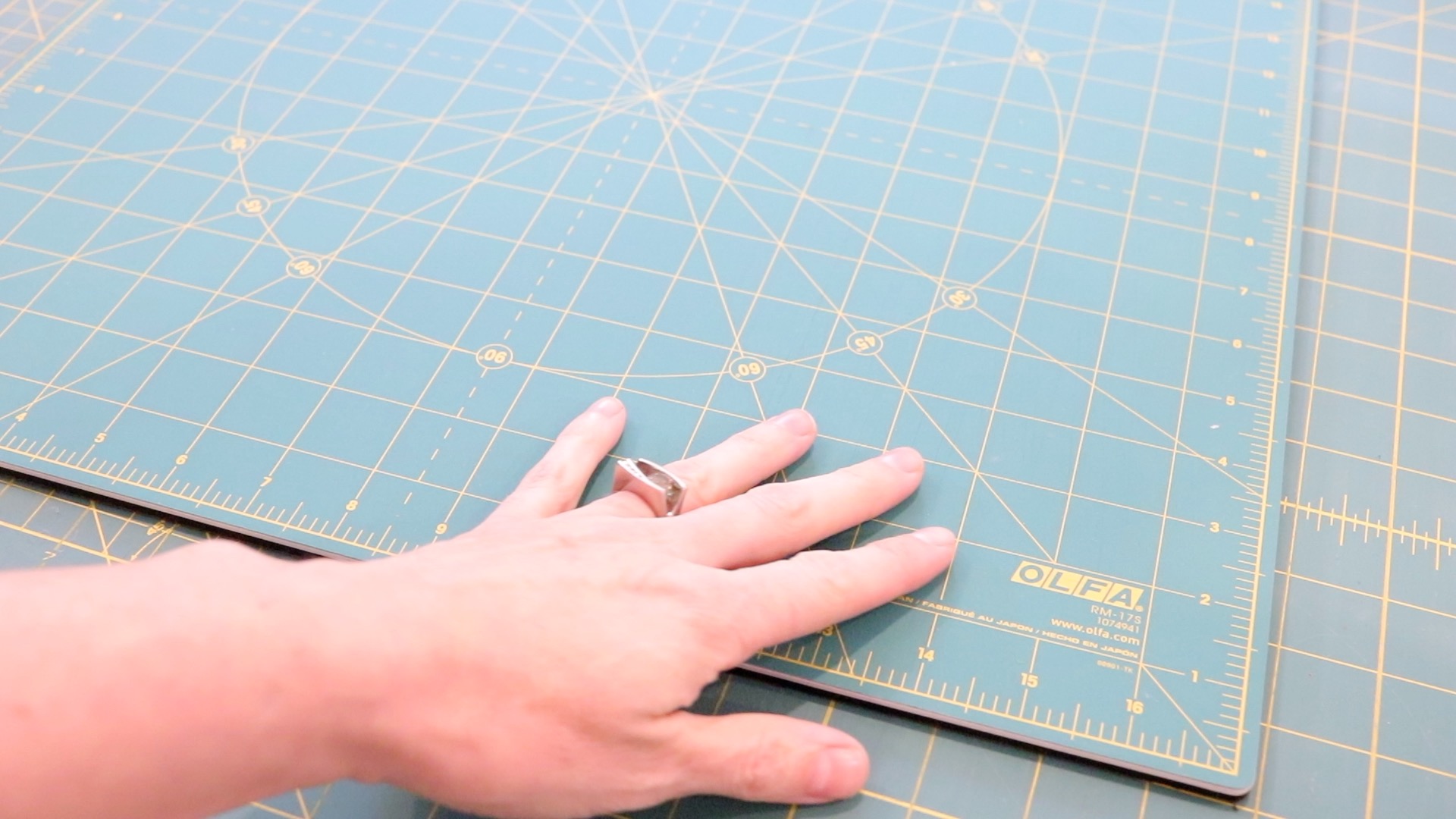 A hand resting onto of a forest green Olfa cutting mat. The mat has visible yellow grid lines for cutting fabric.