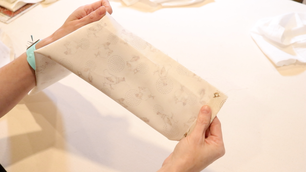 With a magnetic pin bracelet on her hand, a woman is pinning along the long edge of her fabric in preparation for sewing.