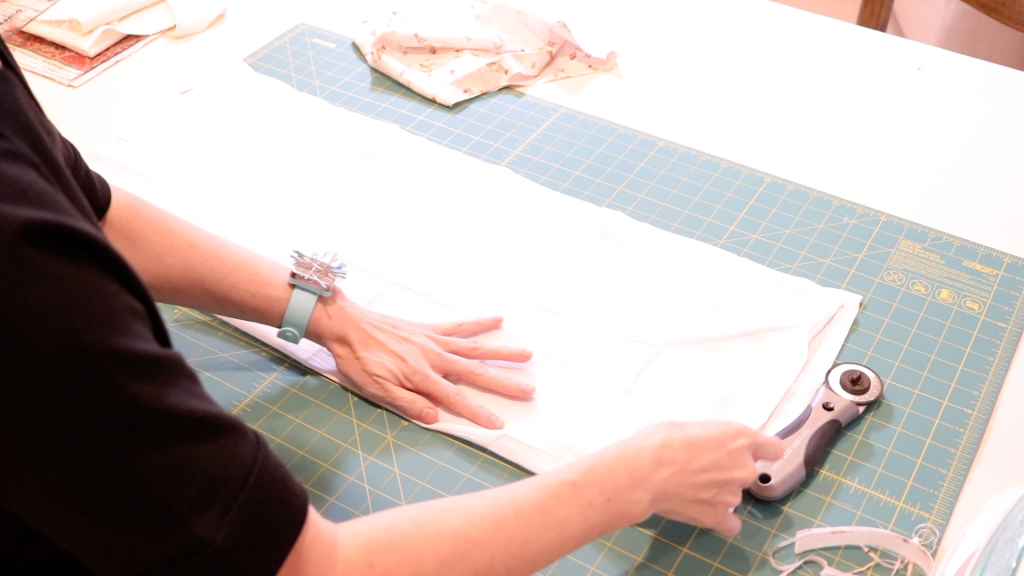 A woman is preparing to cut a piece of white gauze fabric for her sewing project. 