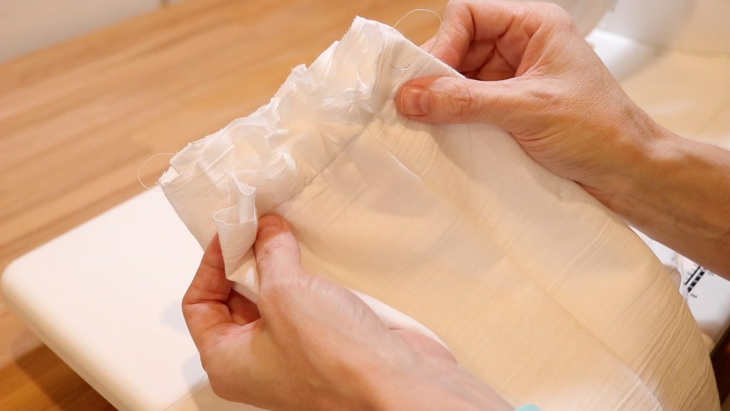 After pinning on the chicken printed fabric to the gauze fabric, a woman is pointing to where she will sew the two pieces together.