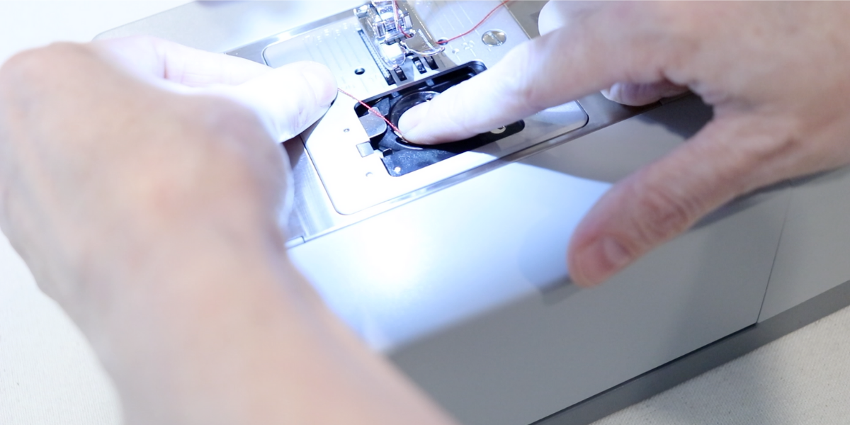 Threading a bobbin case on a gray singer sewing machine.