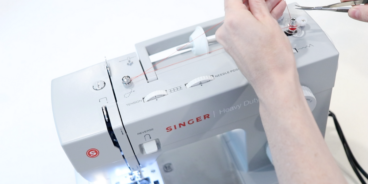 a pair of small thread scissors clipping the red thread once a bobbin winding has begun. 