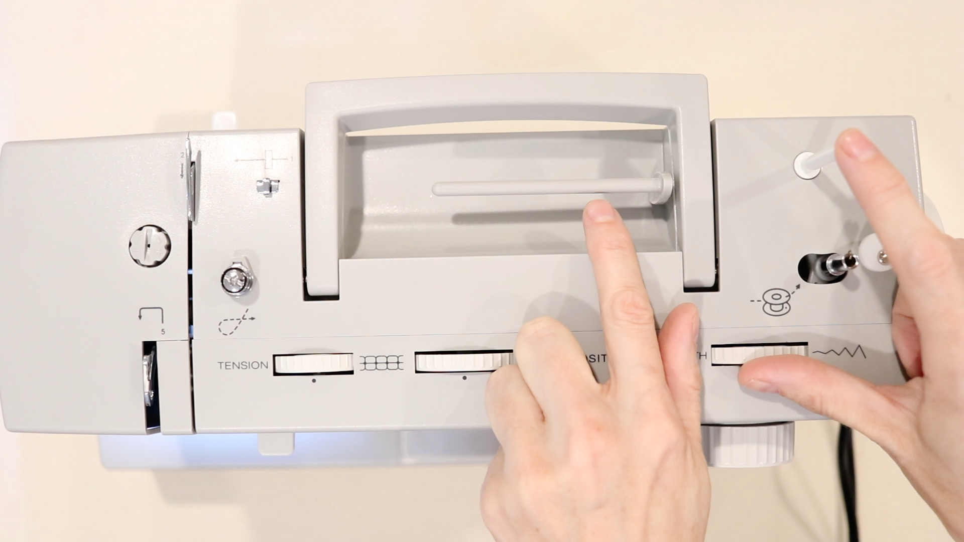 the top of a gray sewing machine pointing to a horizontal spool pin and vertical spool pin on the machine