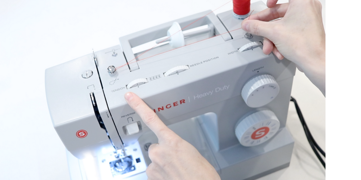 right hand holding the red thread while preparing to thread a machine