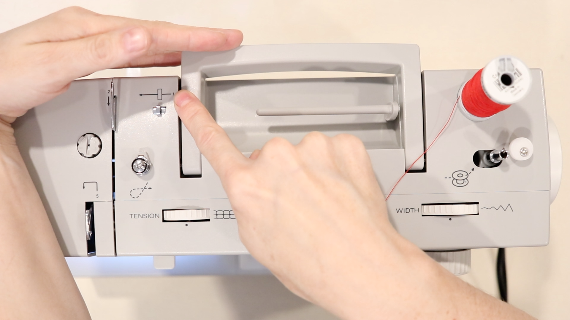 hand pointing to the number 1 on the thread guide on a gray sewing machine.