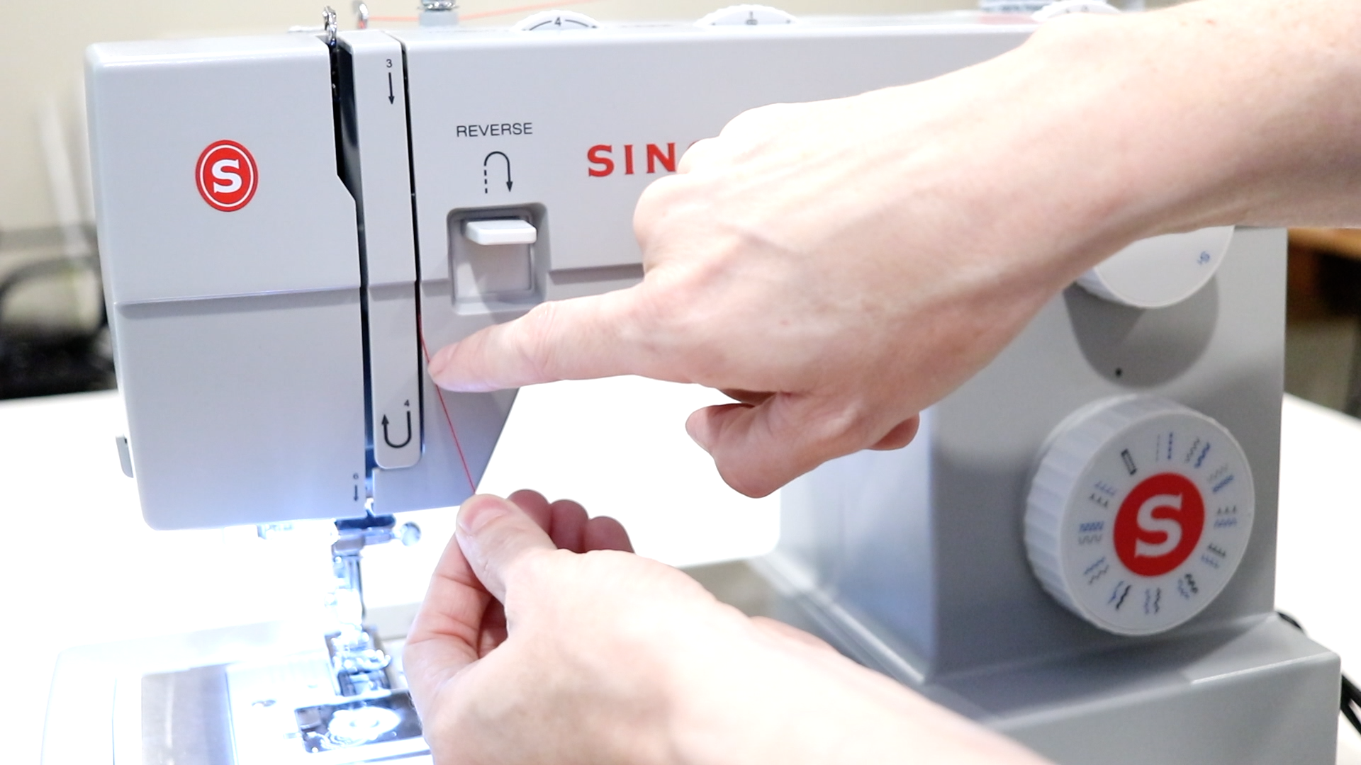 right hand pointing to the take up level threading area on the front of a singer sewing machine.