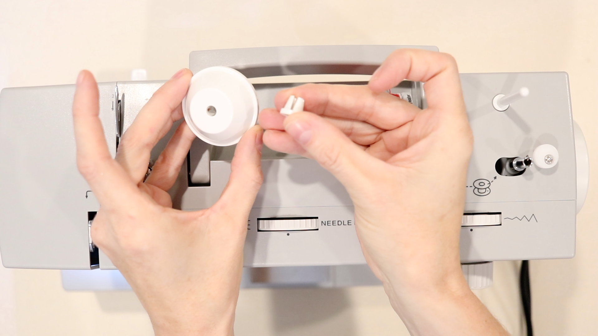 hands holding a spool pin cap and a spool pin to use on a gray sewing machine