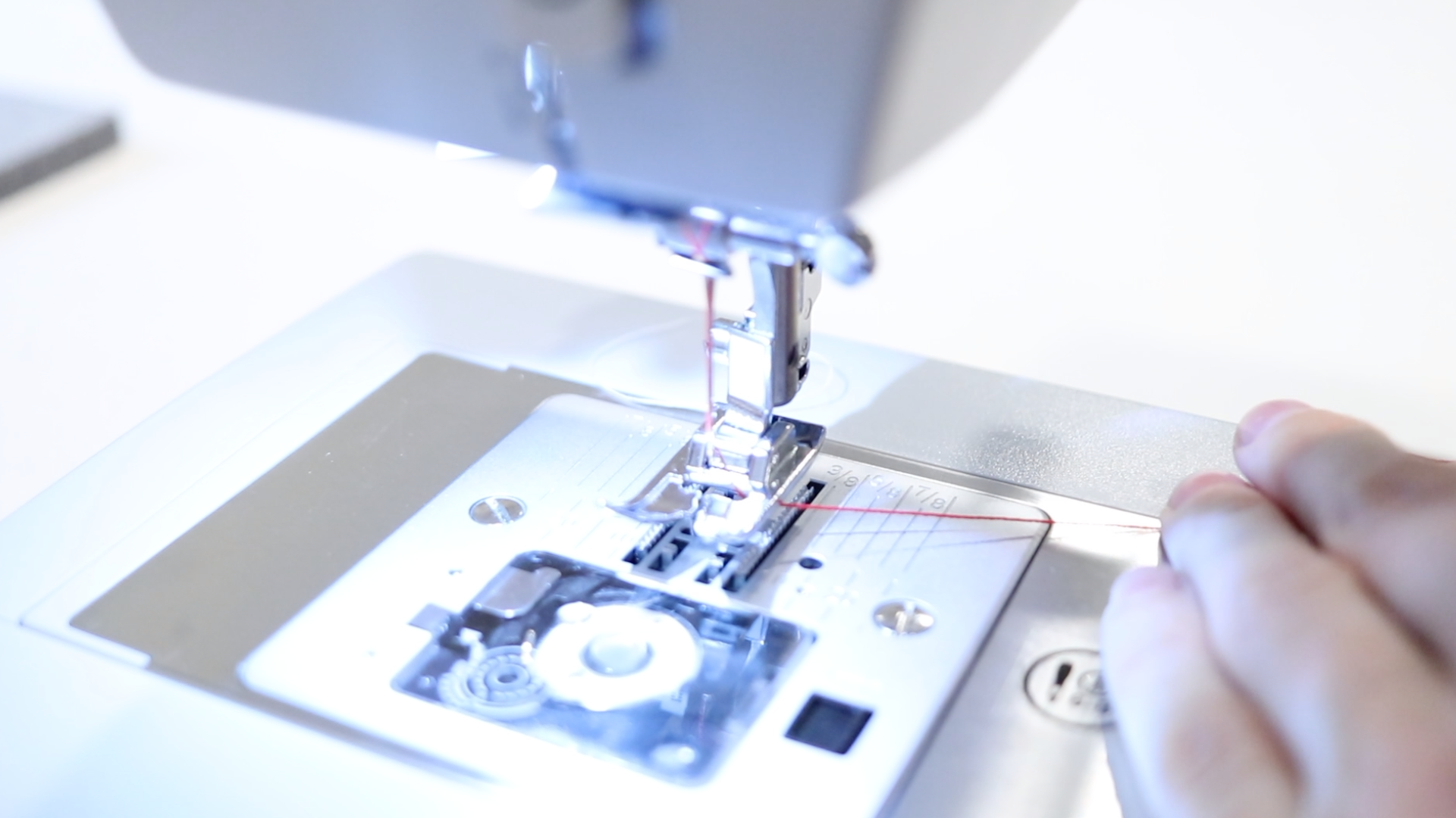 Close up of a sewing machine foot that has been threaded with red thread. 