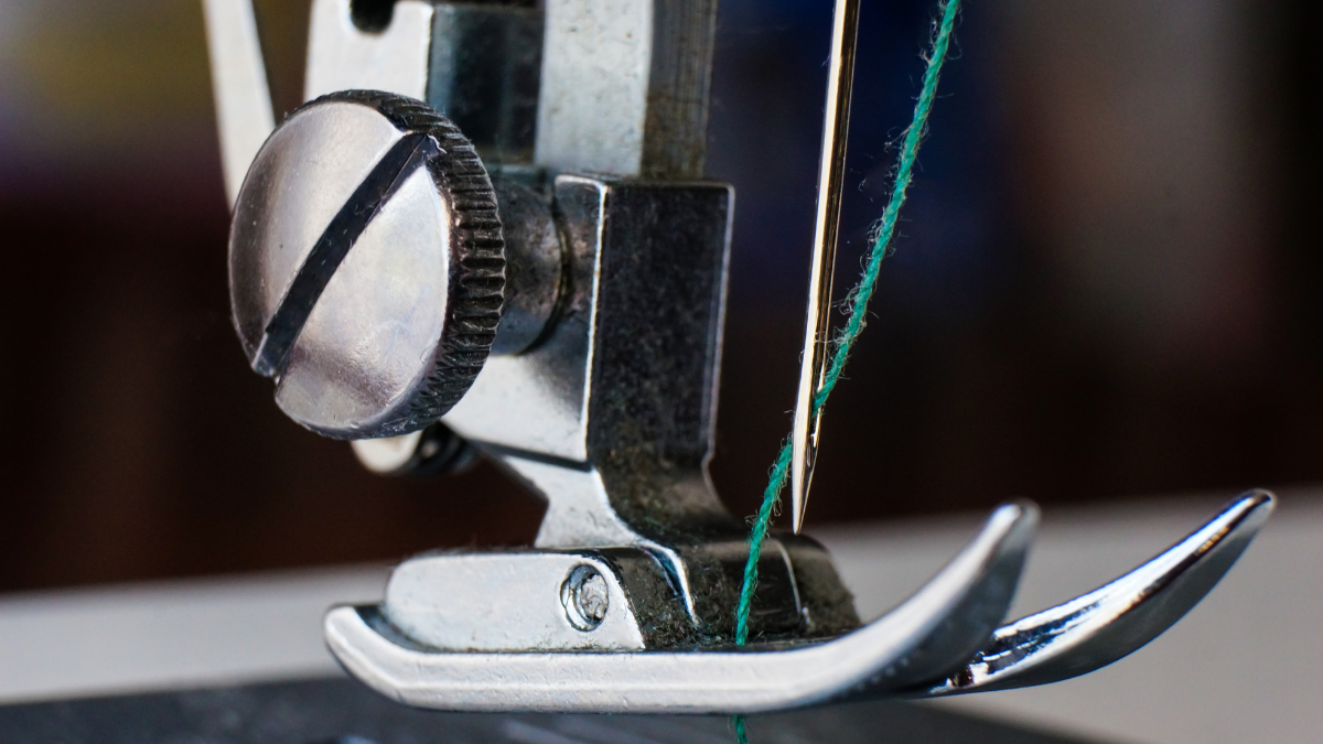 Green thread passing through the center of a sewing machine needle. Close up view of the needle and thread.