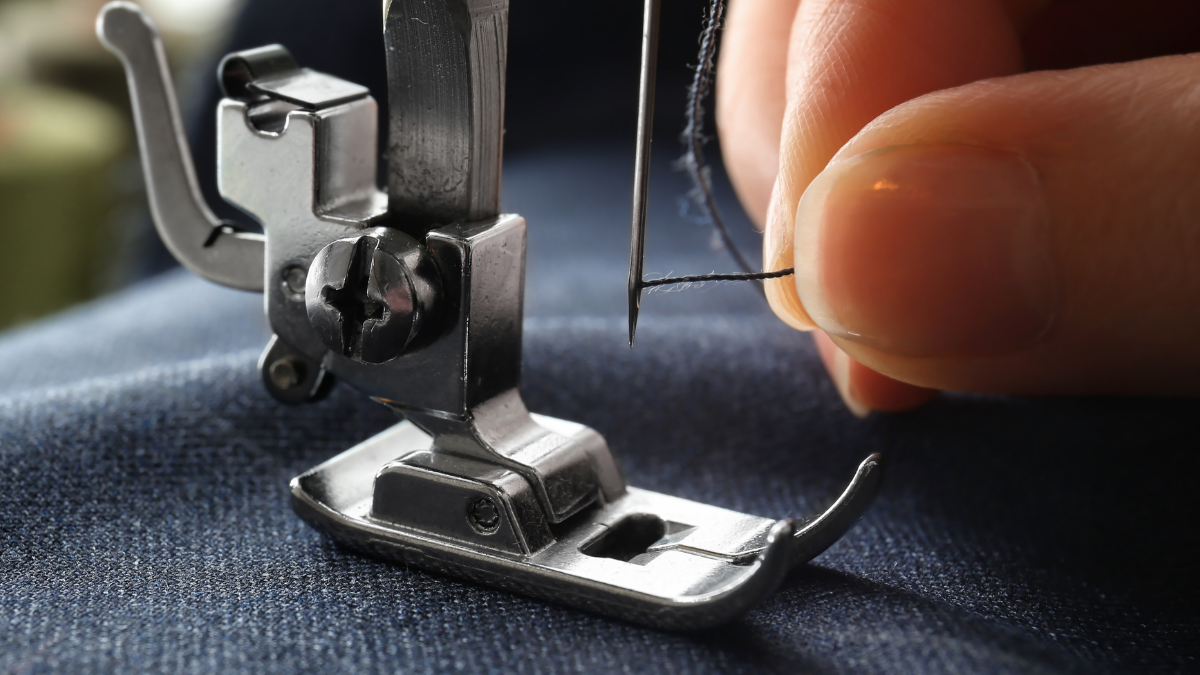 a hand holding a black thread. Its threading a sewing machine needle from front to back