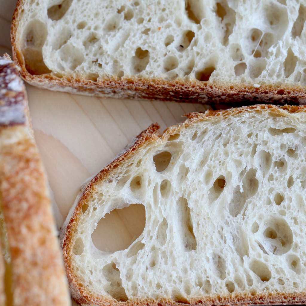 a beautiful loaf of fresh baked sourdough bread sliced into two pieces and placed on a table