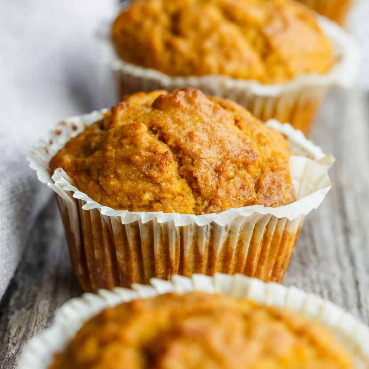 Orange Sourdough Pumpkin Banana muffins wrapped in a paper muffin cup sitting in a uniform line on a plank of old barn wood.
