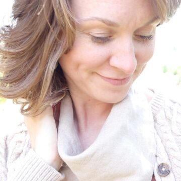 a young lady wearing a tan linen homemade bandana. She is standing outside in the sunshine wearing a light weight tan sweater.