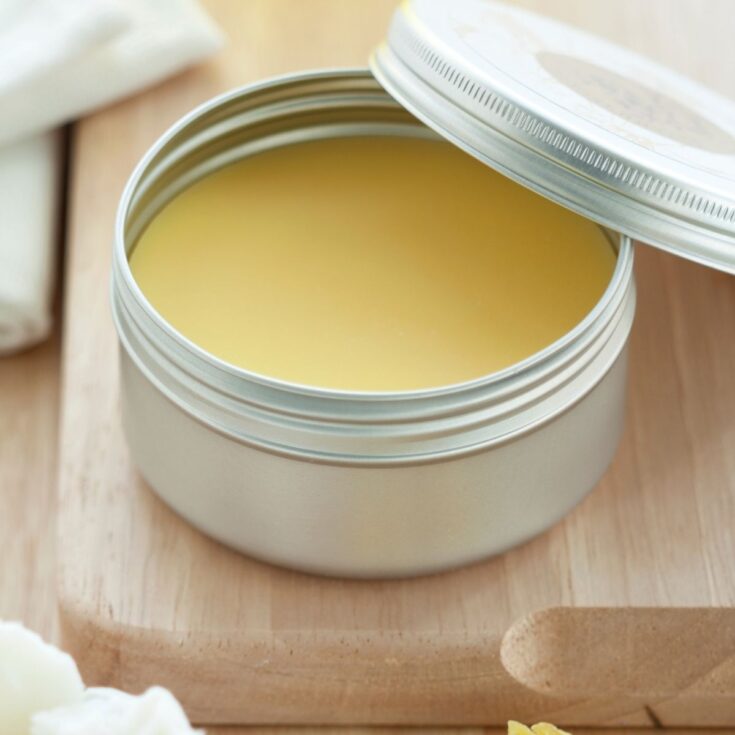 a small silver metal tin filled with a pale yellow cast iron paste. The tin is sitting on a wooden cutting board with the lid sitting perched on the side of this tin