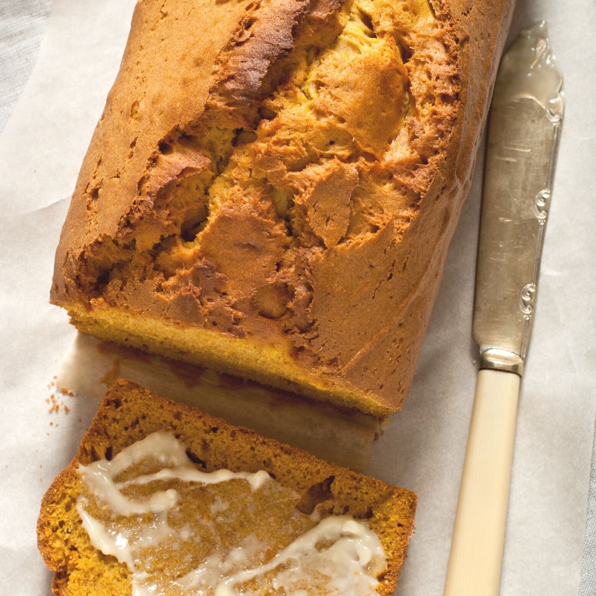 freshly baked sourdough pumpkin banana bread loaf. one piece is sliced off the end and slathered with butter. A vintage butter knife sits nearby with butter on it.