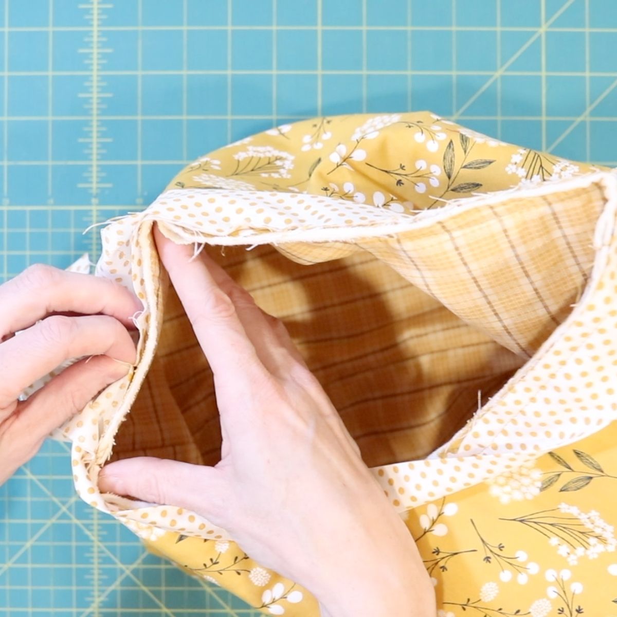 two hands holding a strip of binding fabric close to the raw edge of a fabric basket checking fit before sewing the binding down.