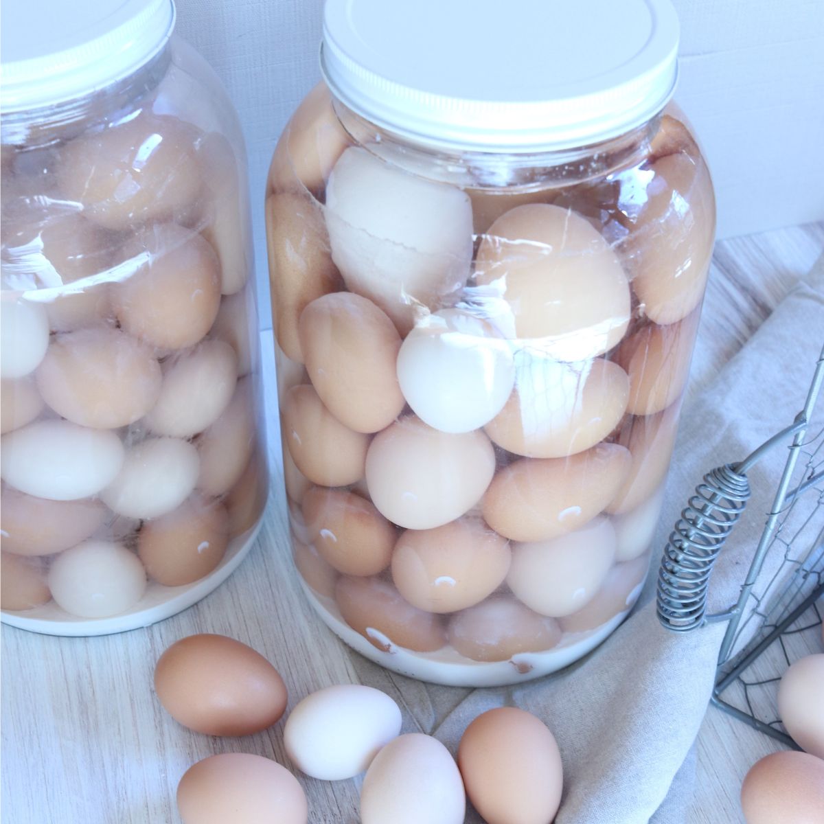 two large clear glass jars full of freshly water glassed eggs using pickling lime. a pile of eggs sits nearby.